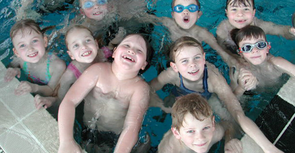 Lachende Kinder im Wasser am Schwimmbeckenrand